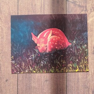 May include: A red fawn with white spots is curled up in a field of green grass and wildflowers. The fawn is sleeping peacefully in the soft light of the setting sun.