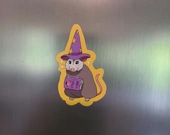 May include: A yellow, cartoon sticker of a gray mouse wearing a purple wizard hat and holding a book that says "Magic Spells".