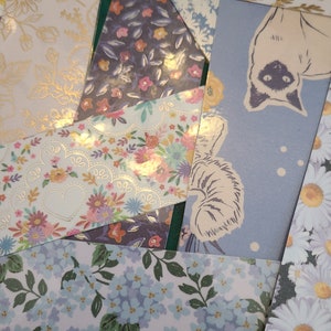 Op de afbeelding: Een verzameling van gepatroneerde papieren restjes met bloemen- en dierenmotieven. De papieren zijn in verschillende tinten blauw, roze en wit.