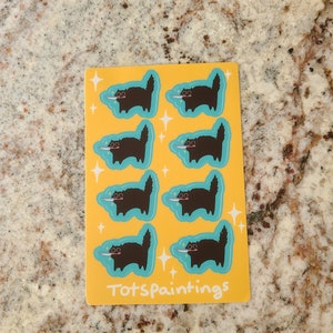 May include: A sheet of eight black cat stickers on a yellow background. Each cat is holding a knife and has a mischievous expression. The stickers are surrounded by small white stars. The sheet is labeled "Totspaintings" at the bottom.