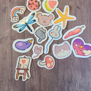 Op de afbeelding: Een verzameling kleurrijke stickers met verschillende schattige dier- en natuurontwerpen. De stickers bevatten een lieveheersbeestje, een watermeloen, een zeester, een vlinder, een muis, een konijn, een kat, een aubergine, een paddenstoel en een regenboog.