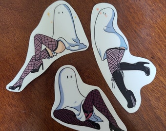 May include: Three white ghost stickers with black fishnet stockings and high heels. The ghosts are in different poses, one is sitting, one is standing with one leg up, and one is standing with both legs straight.