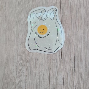May include: A sticker in the shape of a plastic shopping bag with a smiling yellow face and the words "NO THANK YOU" in a circular design. The sticker has a white background and a black outline.