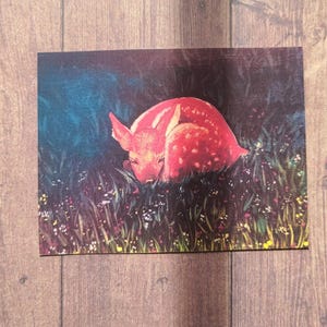 May include: A red fawn with white spots is curled up in a field of green grass and wildflowers. The fawn is sleeping peacefully in the soft light of the setting sun.