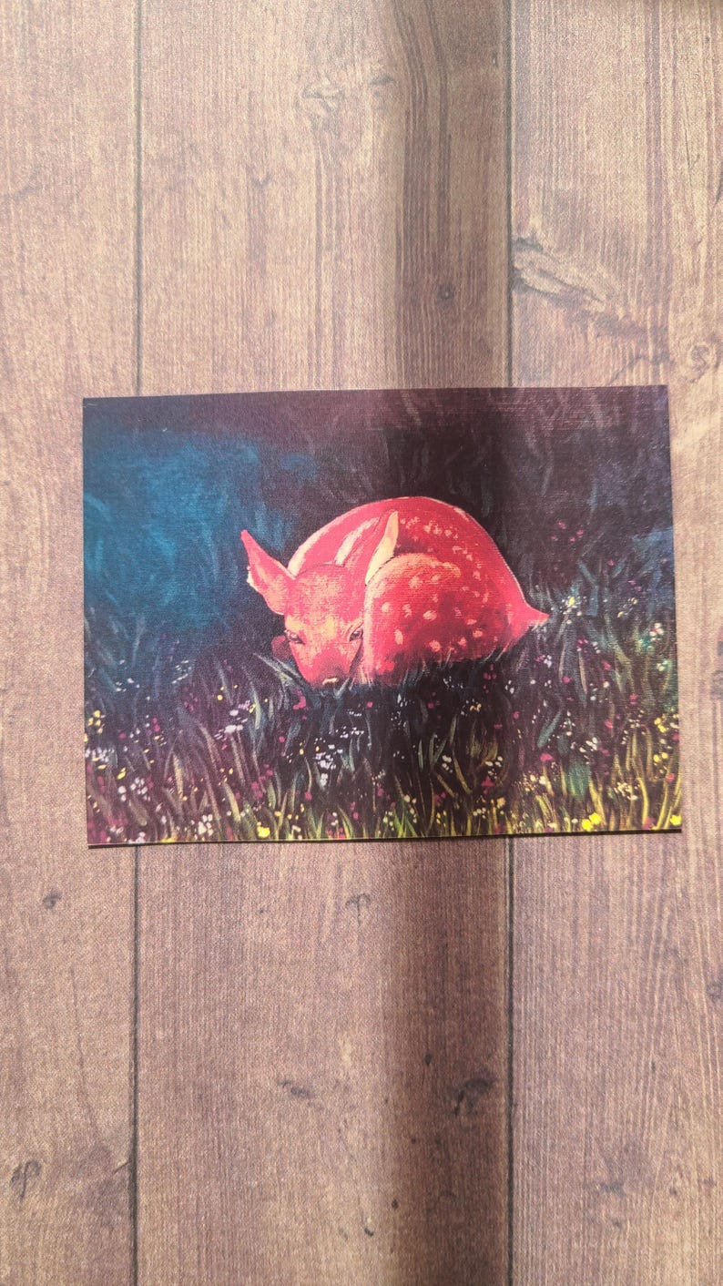 May include: A red fawn with white spots is curled up in a field of green grass and wildflowers. The fawn is sleeping peacefully in the soft light of the setting sun.