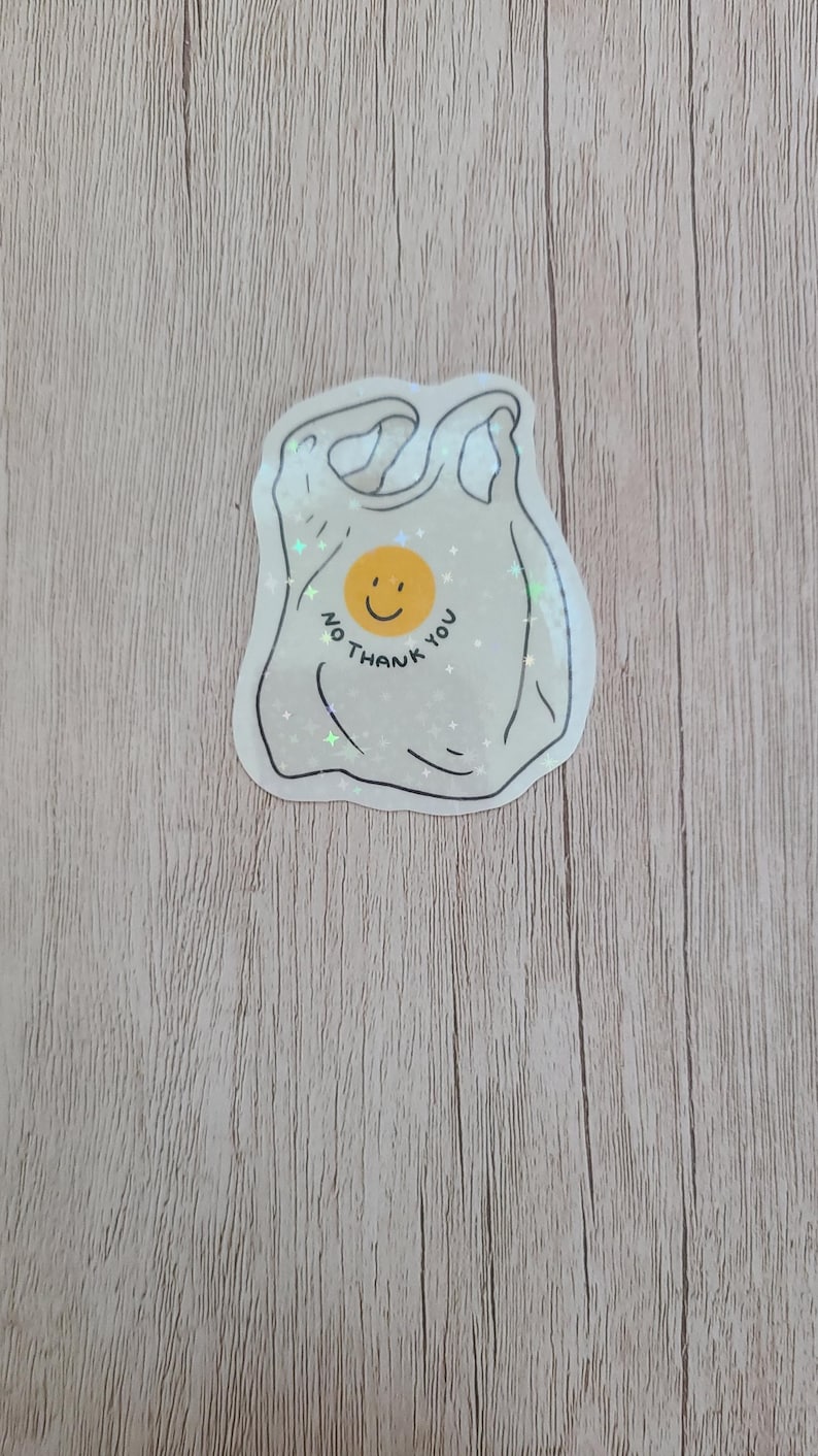 May include: A sticker in the shape of a plastic shopping bag with a smiling yellow face and the words "NO THANK YOU" in a circular design. The sticker has a white background and a black outline.