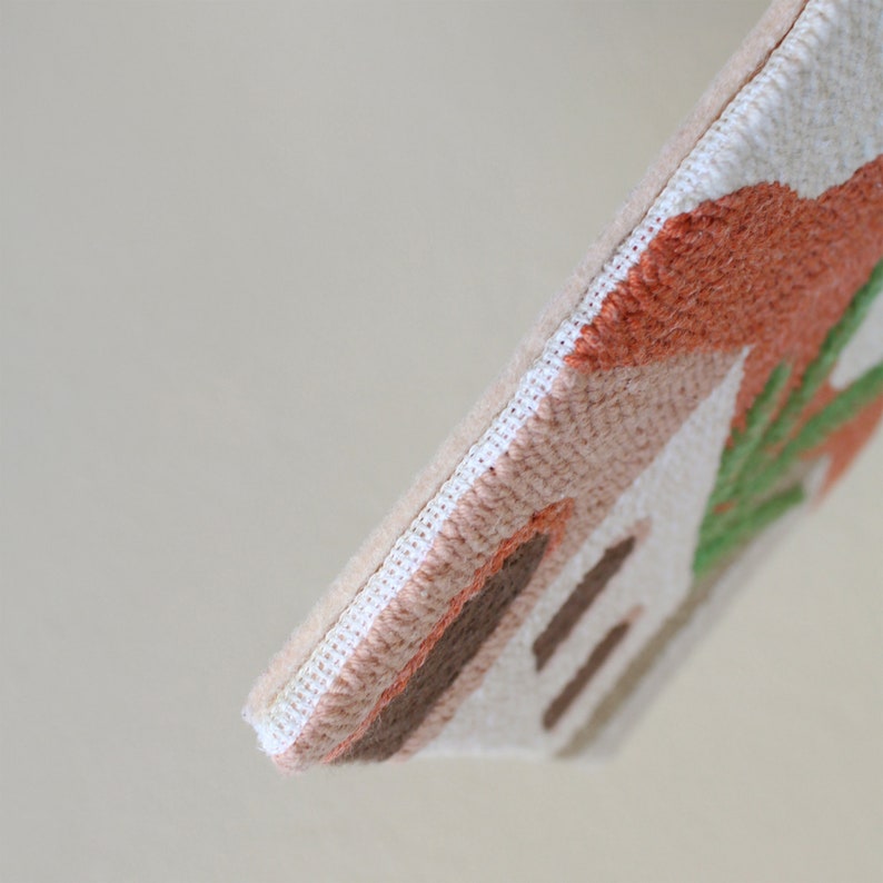 May include: Close-up of a beige fabric pouch with a stitched design of abstract shapes in shades of brown, orange, and green.