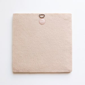 May include: A beige felt board with a silver hanging hook and a pink round sticker that says "remarkable".