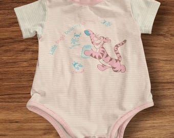 May include: A light pink and white striped baby bodysuit with short sleeves. The bodysuit features a cartoon image of Tigger holding a jar, with the text "Little bugs buzzing around". The trim is pink.