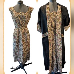 May include: A vintage dress and matching coat set. The dress is sleeveless with a scoop neckline and a floral pattern in shades of beige, green, and pink. The coat is black with floral patterned trim and pockets, and three-quarter sleeves.