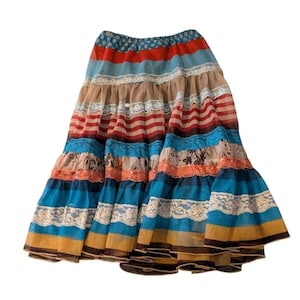May include: A tiered, flowing skirt with a bohemian aesthetic. The skirt features horizontal stripes in various colors, including red, blue, tan, and orange. Lace trim and a polka dot waistband add detail. The skirt is made of a lightweight fabric.