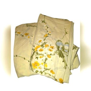 May include: Cream-colored bed sheets with a floral and bird design. The sheets feature yellow and white flowers with green leaves and blue birds. The bedding is folded and appears to be made of a soft fabric.