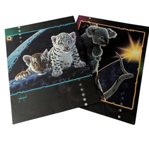 May include: Two art prints featuring animal illustrations. One print shows a tiger cub and a snow leopard cub on a moon-like surface. The other print depicts a koala bear on a branch with a sun in the background. Both prints have a black background with a neon border.