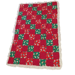 May include: A red and green patchwork quilt with a white lace trim. The quilt features alternating squares of solid red and green patterned fabric. The green squares have a repeating pattern of snowmen and musical instruments.