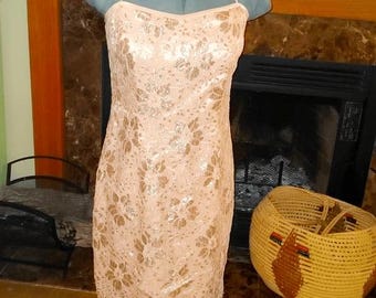 May include: A peach-colored, floral-patterned dress with a halter neckline. The dress is made of lace and has a scalloped hem. The dress is displayed on a mannequin. A woven basket is in the background.
