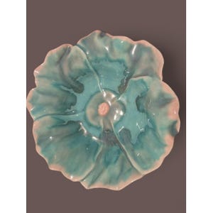 May include: A ceramic, flower-shaped dish with a glossy finish. The dish features a teal interior with a pink center and a pink rim. The petals are textured, and the overall design is reminiscent of a blooming flower. The dish is likely used for decorative purposes.