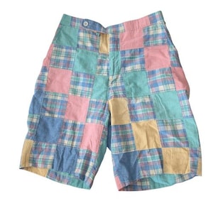 May include: Patchwork shorts in pastel colors. The shorts feature a patchwork design with squares of pink, blue, yellow, and teal plaid fabric. The shorts have a button closure and a classic fit, perfect for a casual summer look.
