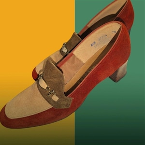 May include: A pair of vintage women's shoes with a color-block design. The shoes feature a red suede body, a tan suede toe, and a brown suede accent with a silver buckle. The heel is a stacked wooden block heel.