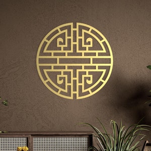 Könnte beinhalten: Ein goldenes geometrisches Design in Form eines Kreises befindet sich an einer braunen Wand. Das Design ist ein traditionelles chinesisches Symbol. Im Vordergrund befindet sich ein Holzstuhl mit einem geflochtenen Sitz und ein Holzschränkchen mit geflochtenen Türen.