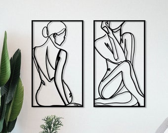 May include: Two black and white line art prints of a woman's figure. The prints are framed in black and are hanging on a white wall.