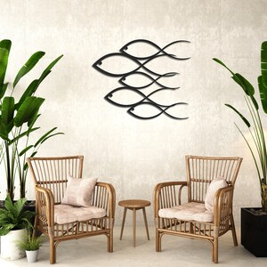 May include: Two wicker chairs with cushions sit in front of a wall with a black metal wall art sculpture of fish. The wall art is made of five fish, each with a curved body and a tail that flows into the next fish. The fish are arranged in a staggered pattern, with the largest fish at the top and the smallest fish at the bottom.