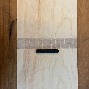 May include: A light wood clipboard with a black metal handle and a row of holes along the top edge.