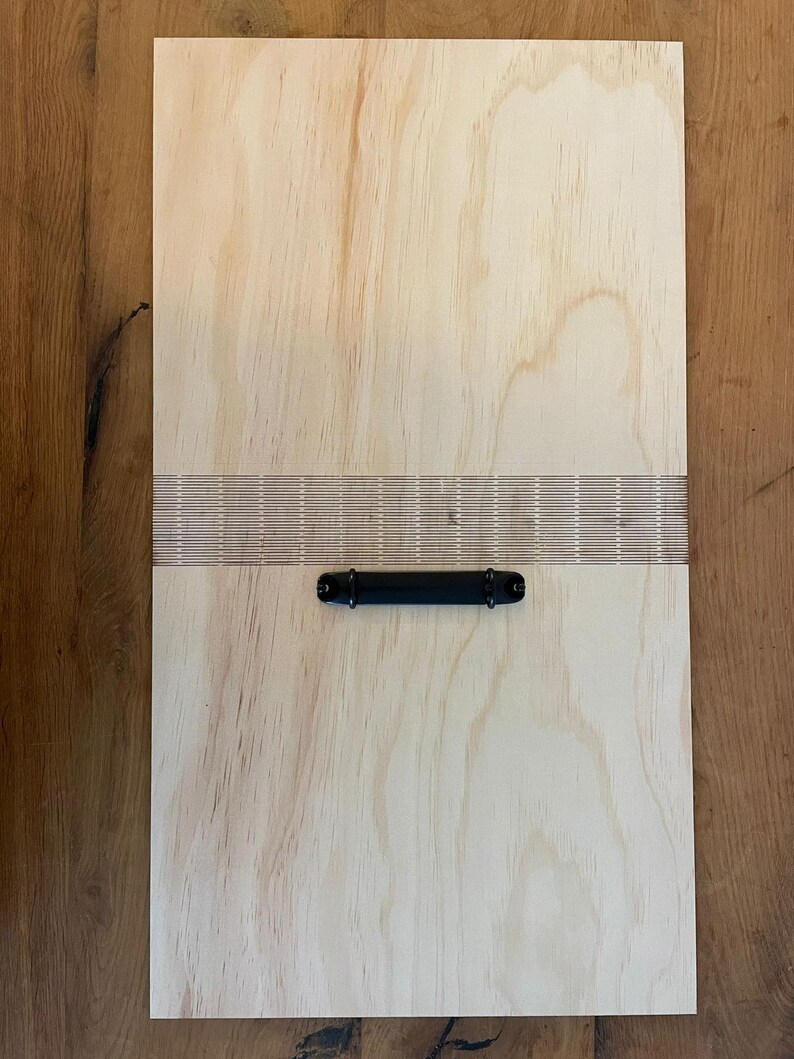 May include: A light wood clipboard with a black metal handle and a row of holes along the top edge.