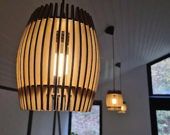 May include: Three wooden pendant lights with a slatted design hang from the ceiling. The lights are illuminated and cast a warm glow. The lights are in a room with a window and plants.