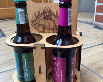 May include: A wooden beer caddy with a laser-engraved firefighter graphic on the center panel, holding two dark glass bottles. The left bottle has a teal label and cap, while the right bottle features a magenta label and cap, both with barcodes.
