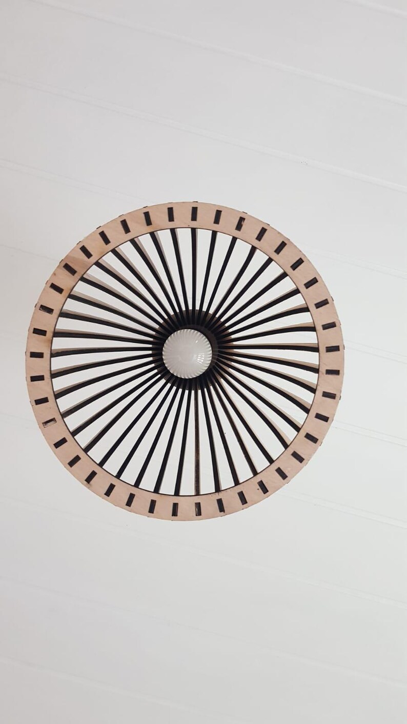 May include: A circular pendant light fixture featuring a light-colored wooden outer ring and a series of dark, thin, radiating spokes that converge toward a central white light bulb, creating a geometric, sunburst-like pattern.