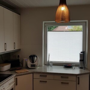 May include: A kitchen interior featuring white cabinets with silver handles, a speckled gray countertop, and a wooden slatted pendant light hanging above. A window with white pleated blinds, a food processor, and a toaster are visible.