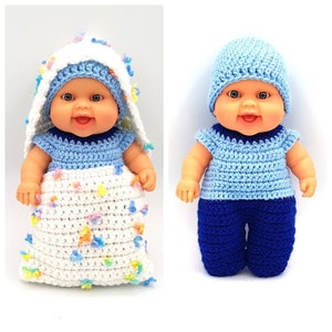 May include: Two crocheted baby doll outfits. One outfit is a white sleeping bag with colorful flowers and a blue crocheted hat. The other outfit is a blue crocheted shirt and blue pants with a blue crocheted hat.