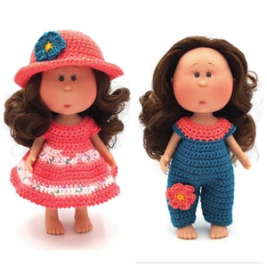 May include: Two crocheted dolls with brown hair. One doll is wearing a pink dress with a white flower pattern and a pink hat with a blue flower. The other doll is wearing a blue jumpsuit with a pink flower.