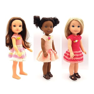 May include: Three dolls wearing crocheted dresses. The dresses are pink, peach, and red with white accents. The dolls have brown, black, and blonde hair.