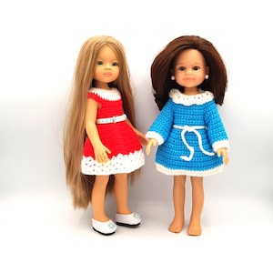 Peut inclure: Deux poupées portant des robes en crochet. La poupée de gauche porte une robe rouge avec des bordures blanches et une ceinture blanche. La poupée de droite porte une robe bleue avec des bordures blanches et une ceinture blanche.