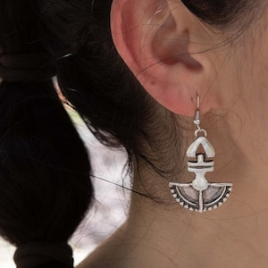 May include: Silver earrings with a geometric design. The earrings are shaped like a crescent moon with a small triangle on top. The earrings are hanging from a person's ear.