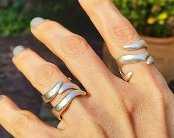 May include: Two silver rings with a wavy, organic design. The rings are worn on the middle and ring fingers of a hand.