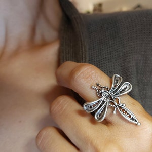 以下が含まれることがあります： 銀製のフィリグリー蜻蛉のリング。リングは細部までこだわった複雑なデザインで、繊細なデザインです。