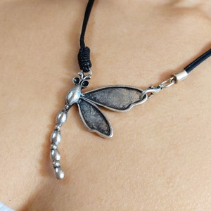 May include: A silver dragonfly pendant necklace with a black cord. The dragonfly has a beaded tail and detailed wings.