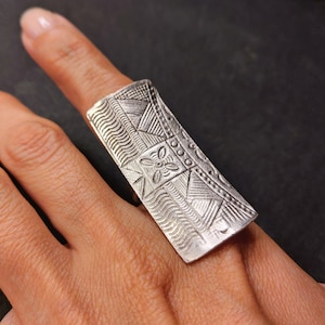 Op de afbeelding: Een zilveren ring met een ingewikkeld geometrisch ontwerp. De ring is breed en plat en heeft een bloemmotief in het midden.