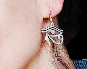 May include: Silver-toned metal earrings featuring the Eye of Horus symbol. The earrings have a hook closure and a detailed design, showcasing the ancient Egyptian symbol's iconic elements. The earrings are worn on the ear.