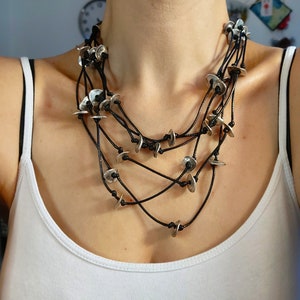 May include: A layered necklace with multiple strands of black cord and silver disc pendants.