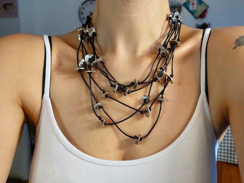 May include: A layered necklace with multiple strands of black cord and silver disc pendants.