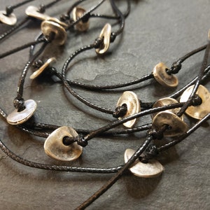 May include: A multi-strand necklace with silver-toned metal beads and black cord. The beads are shaped like small, flat discs with a hole in the center.