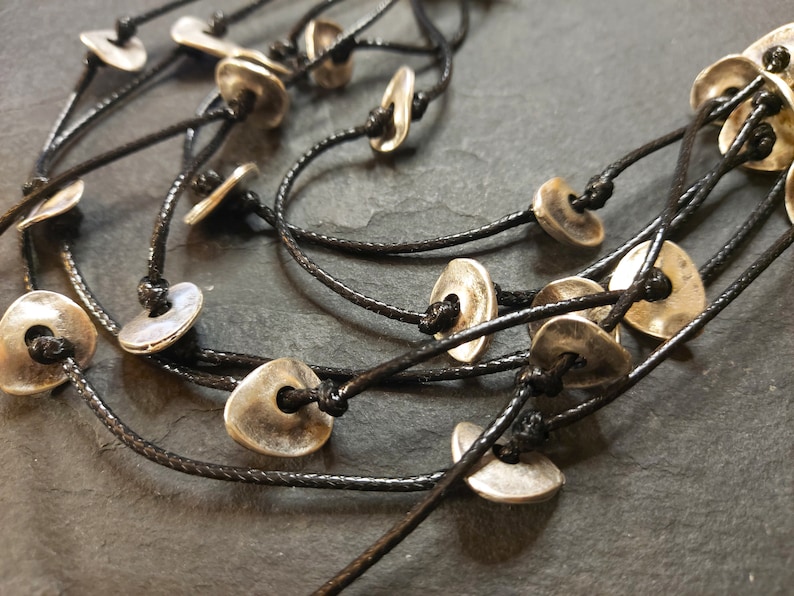 May include: A multi-strand necklace with silver-toned metal beads and black cord. The beads are shaped like small, flat discs with a hole in the center.