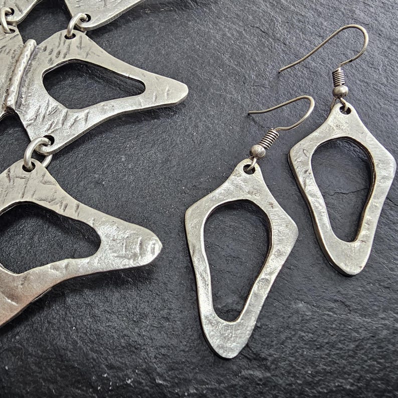 Anatomical silver necklace and matching earrings collection flatlay dark stone, handmade sculptural silver plated geometric jewelry set, wearable art by Gozemre Atelier