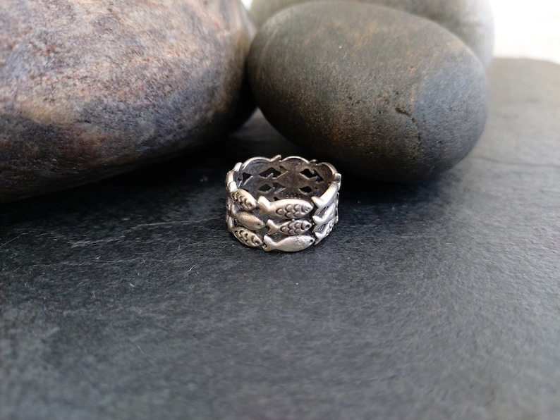 May include: A silver ring with a design of multiple fish swimming in a circle.
