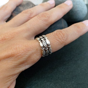 May include: A silver ring with three bands of fish designs. The ring is on a person's finger.