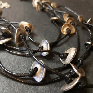 May include: A multi-strand necklace with silver-toned metal disc pendants and black cord.