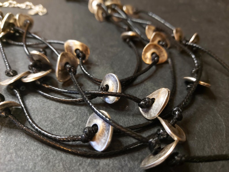 May include: A multi-strand necklace with silver-toned metal disc pendants and black cord.